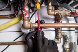 Person in black gloves using a screwdriver on a complex plumbing system.