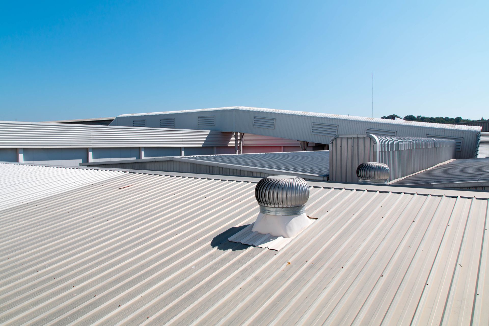 A corrugated metal roof under a bright blue sky, featuring a metallic ventilation turbine and a long, sloped structure.