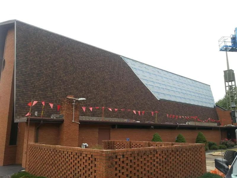 A brick building with a partially shingled, partially under-construction roof, adorned with red pennant flags.