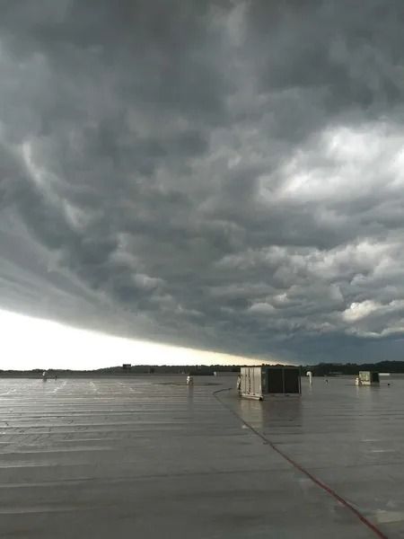A flat rooftop under a vast, dark, and dramatic storm cloud formation stretching across the horizon.