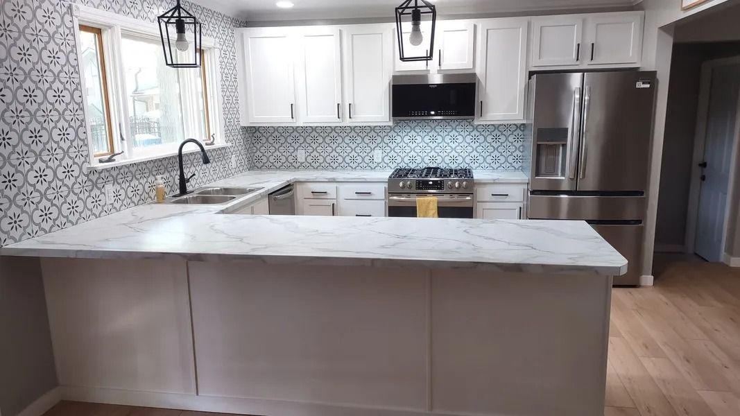 A renovated kitchen with white cabinets, marble-look countertops, a stainless steel refrigerator, and patterned backsplash.