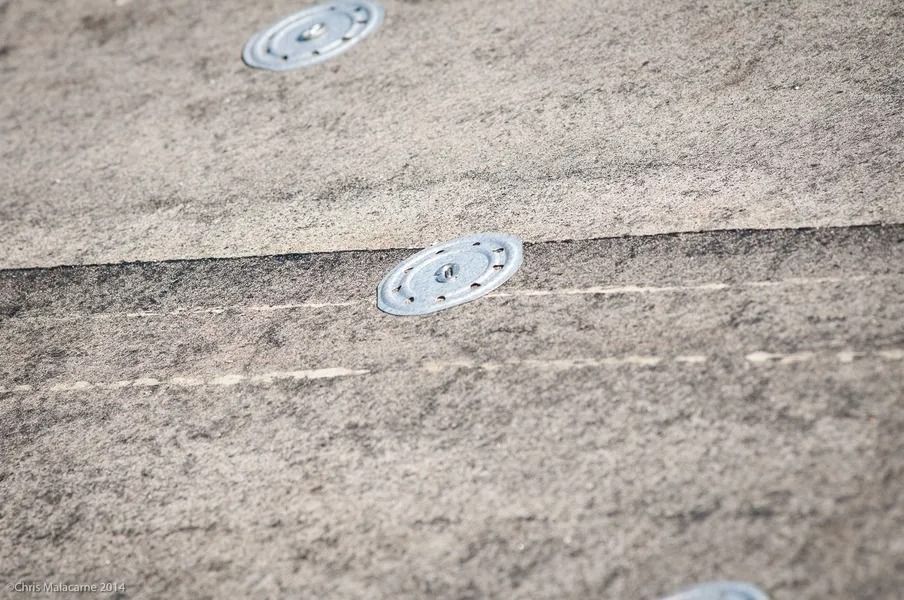 Metal insulation fasteners secured on a textured, gray commercial roofing surface.