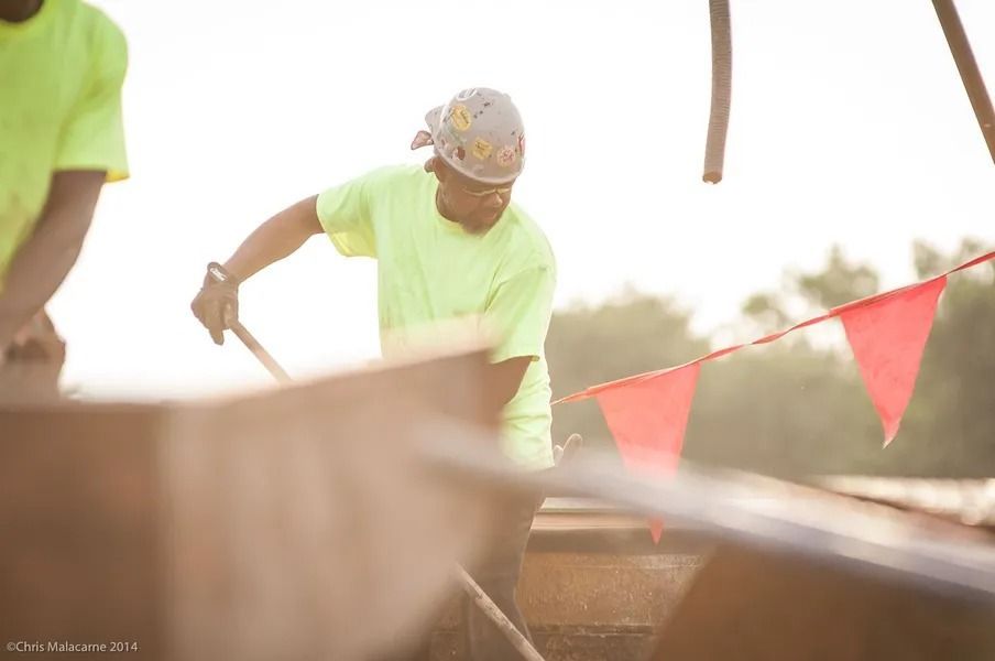 Construction workers in neon yellow shirts work on a metal structure adorned with red triangular flags at sunset.