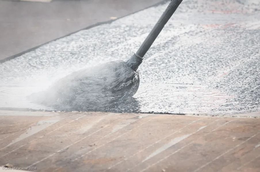 A mop cleaning a wet, textured dark grey surface next to a tan stone floor.