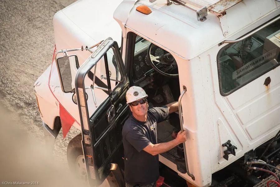 A person wearing a hard hat smiles while standing at the open door of a white industrial truck.