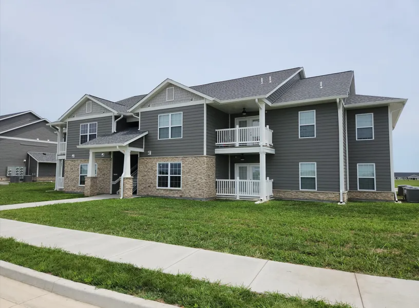 A two-story apartment building with dark grey siding, stone accents, white trim, and balconies under a clear sky.