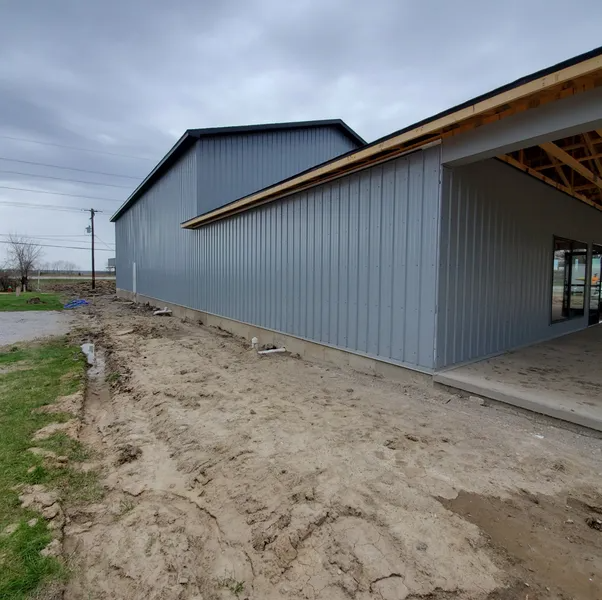 A gray metal-sided building under construction with a dirt ground and an open entryway on the right.