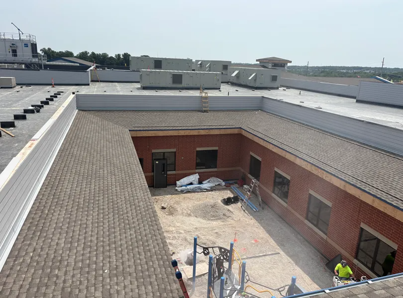 An elevated view of a brick building’s inner courtyard, showing shingled roofing, roof-mounted HVAC units, and debris.