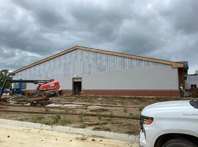 Construction site featuring a partially sided building with a brick base, a boom lift, and a white pickup truck.