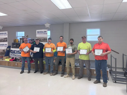 Seven people standing in a row on a stage indoors, holding awards and facing the camera for a group photo.