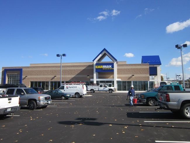 A CarMax dealership building with cars parked in the lot under a blue sky on a sunny day.