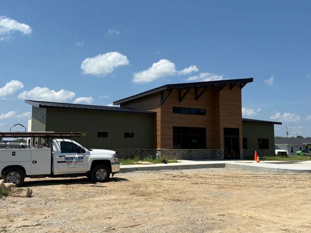 A modern, single-story commercial building with tan siding and wood-style accents, featuring a white work truck in front.