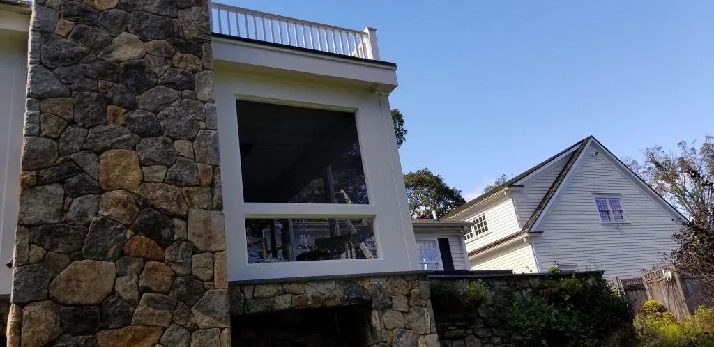 A multi-story house with stone chimney and large windows on a sunny day.