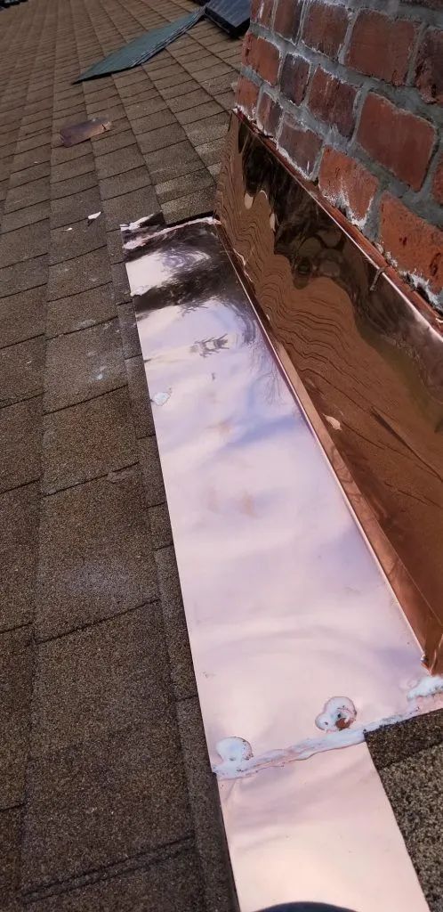 Copper flashing installed around a brick chimney on a shingle roof.