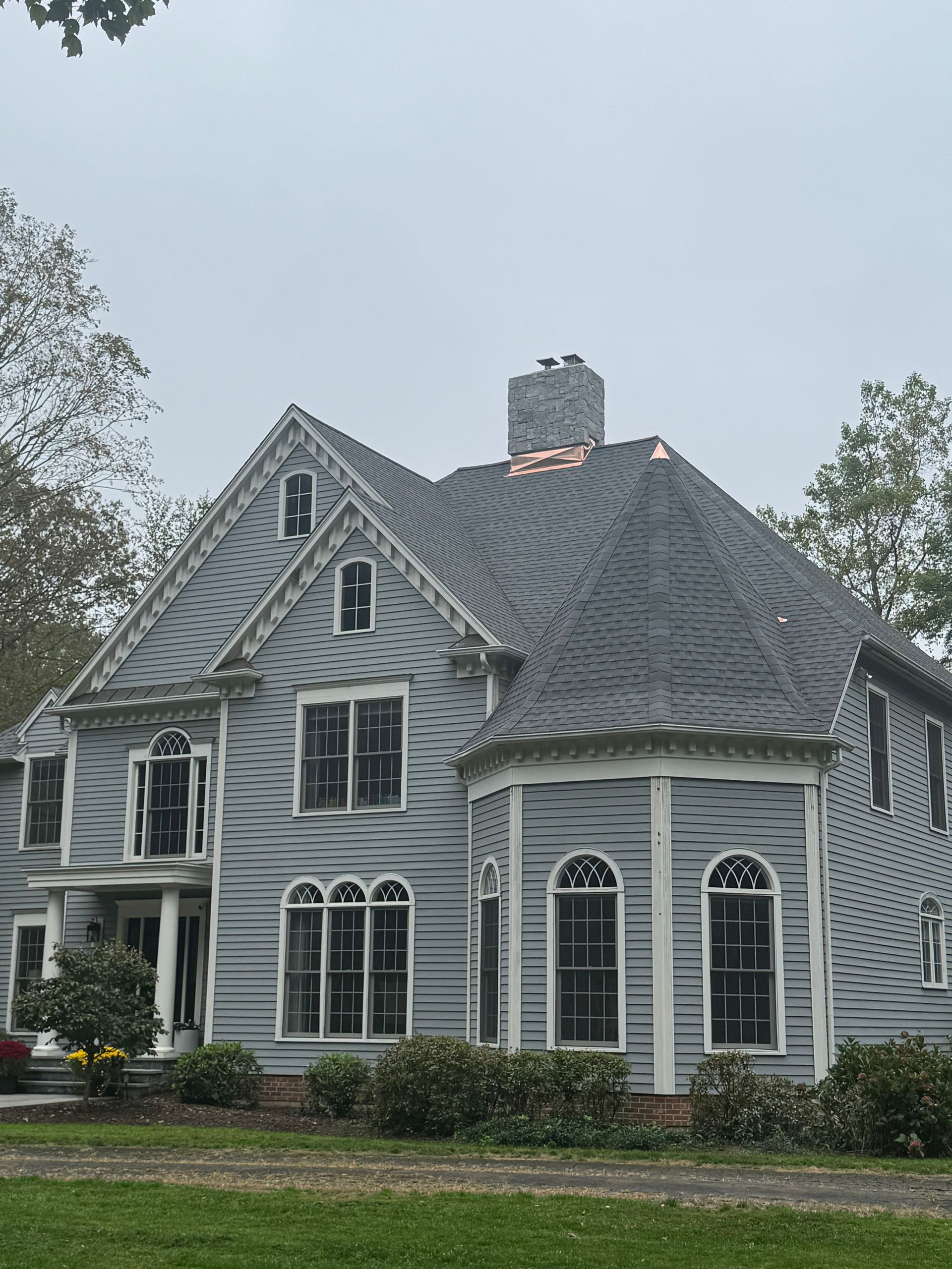 Gray house with dark roof and multiple windows under a cloudy sky.