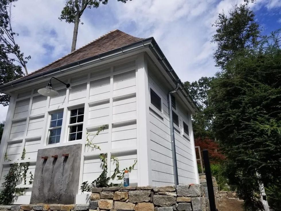 White wooden structure with a red tile roof, set among trees against a blue sky.