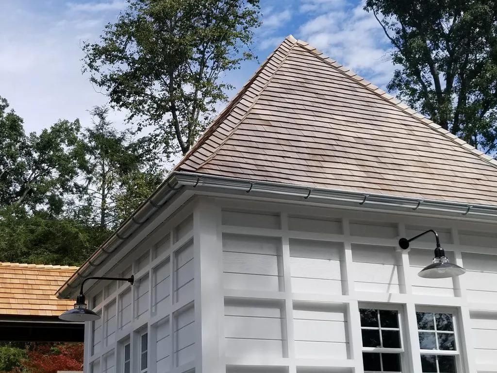White building with grid-patterned walls and brown shingle roof, outdoor lights, set against trees.