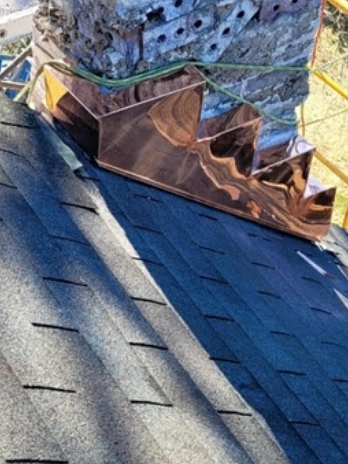 Copper flashing installed around a chimney on a dark shingle roof.