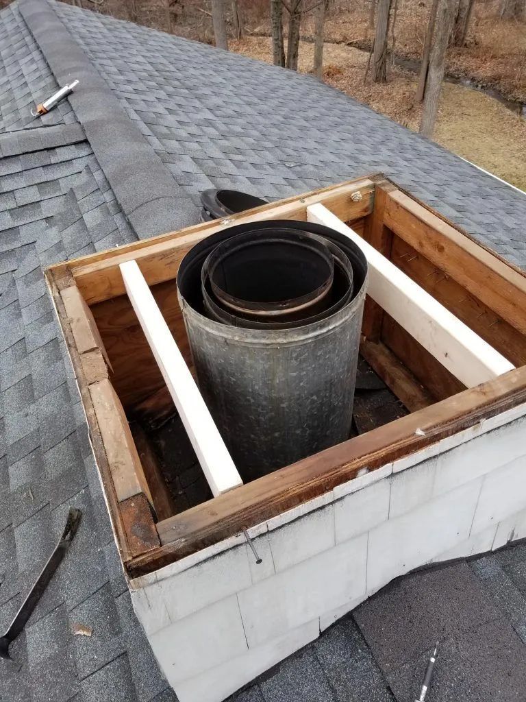 Chimney under construction with exposed metal flue surrounded by wooden frame, on a shingled roof.