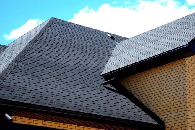 Dark shingle roof against a blue sky, over light brick exterior and black gutters.