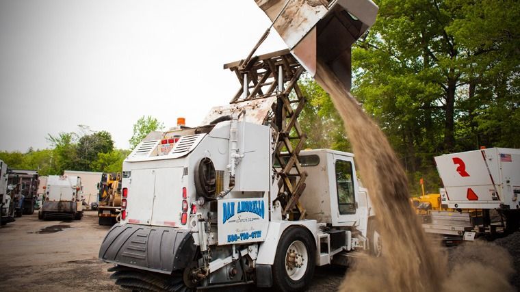 White utility truck unloading dirt from a raised bed at a worksite