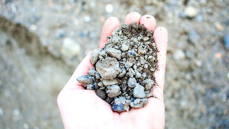 Hand holding a small pile of gravel and dirt over a rocky ground