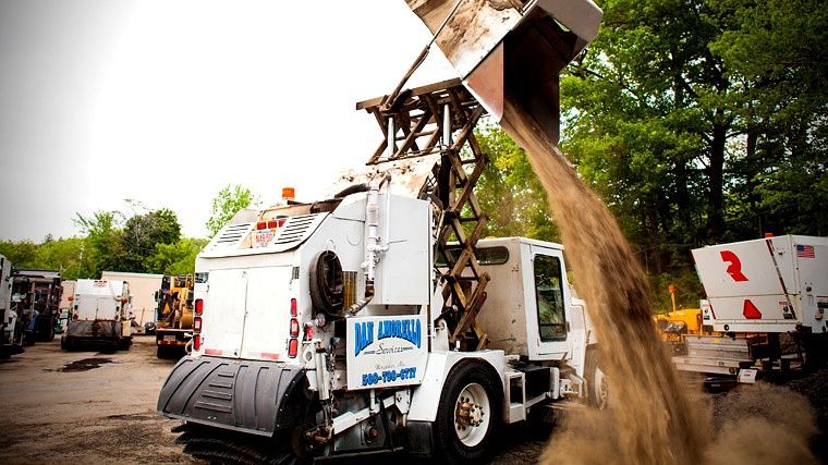White garbage truck dumping debris into a large pile at an outdoor construction site