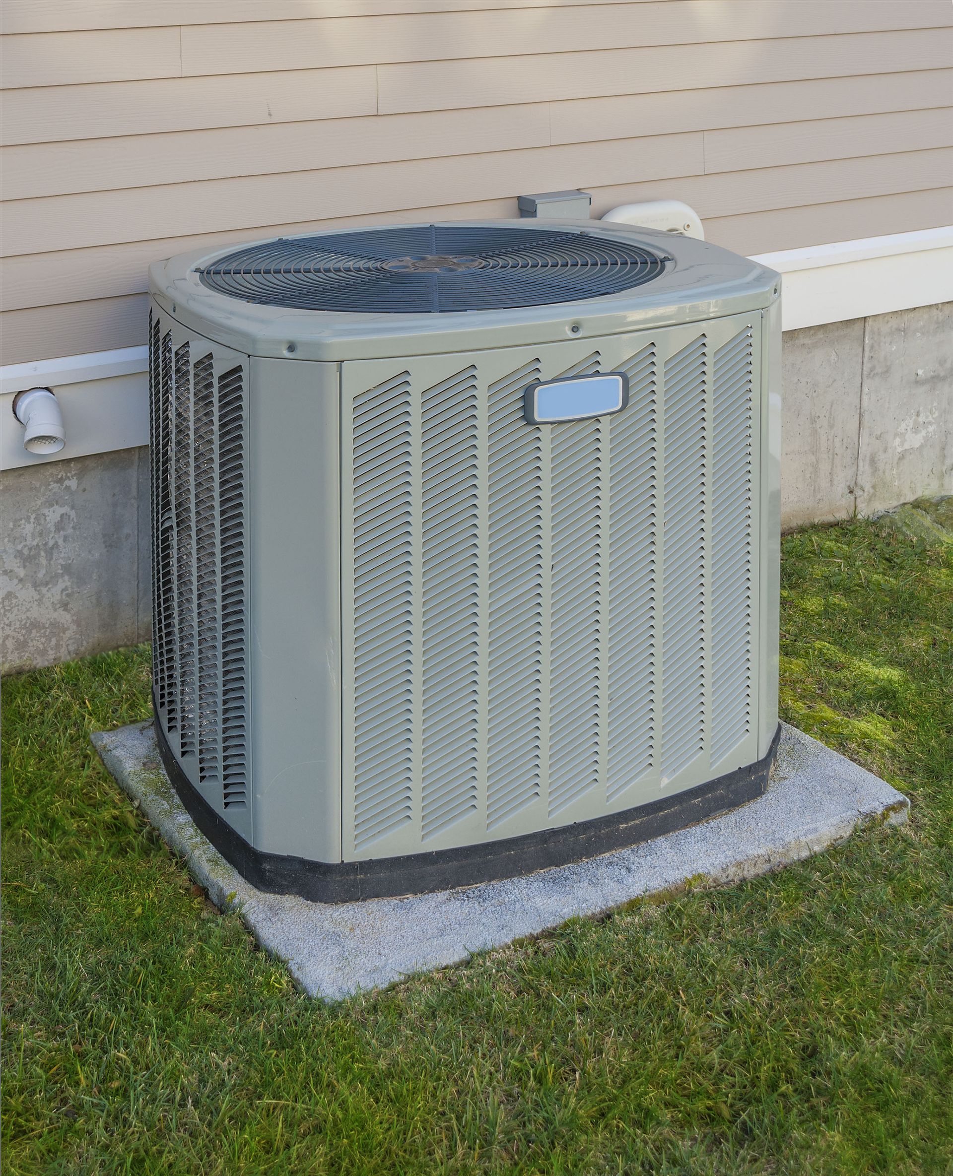 An air conditioning unit, gray, on a concrete pad, outside a house.