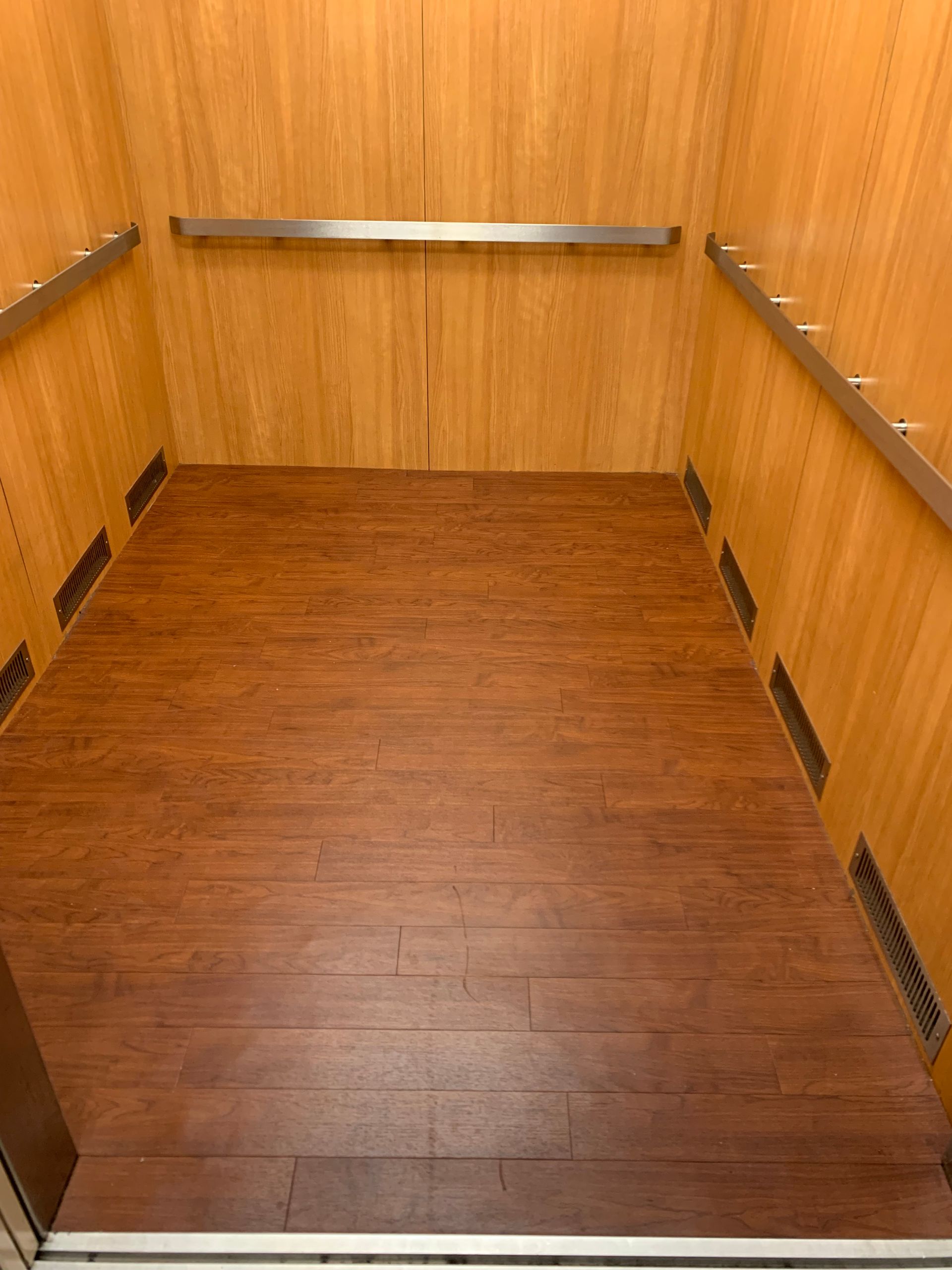 The inside of an elevator with wooden walls and a wooden floor.