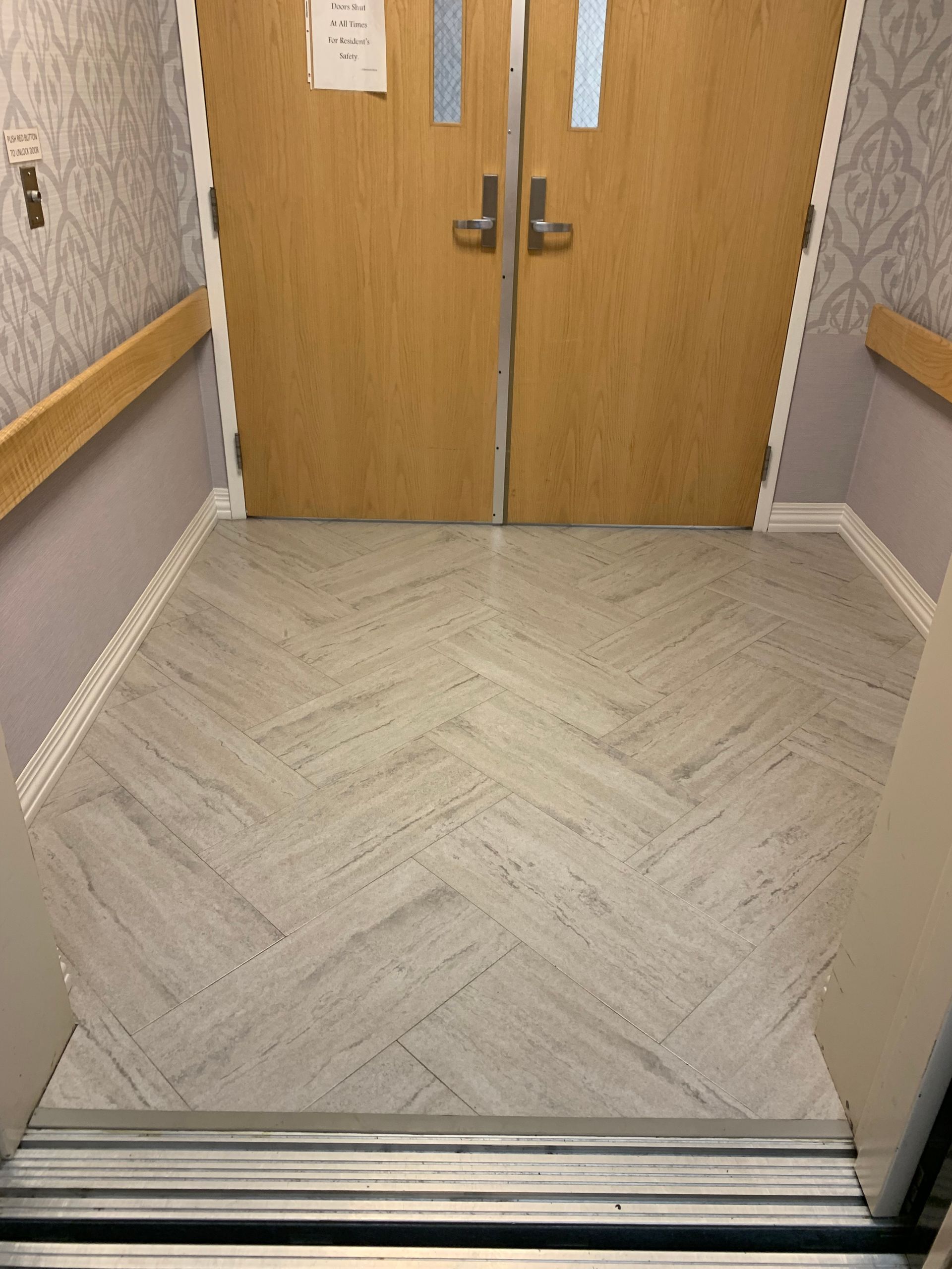 A hallway with a herringbone floor and wooden doors.