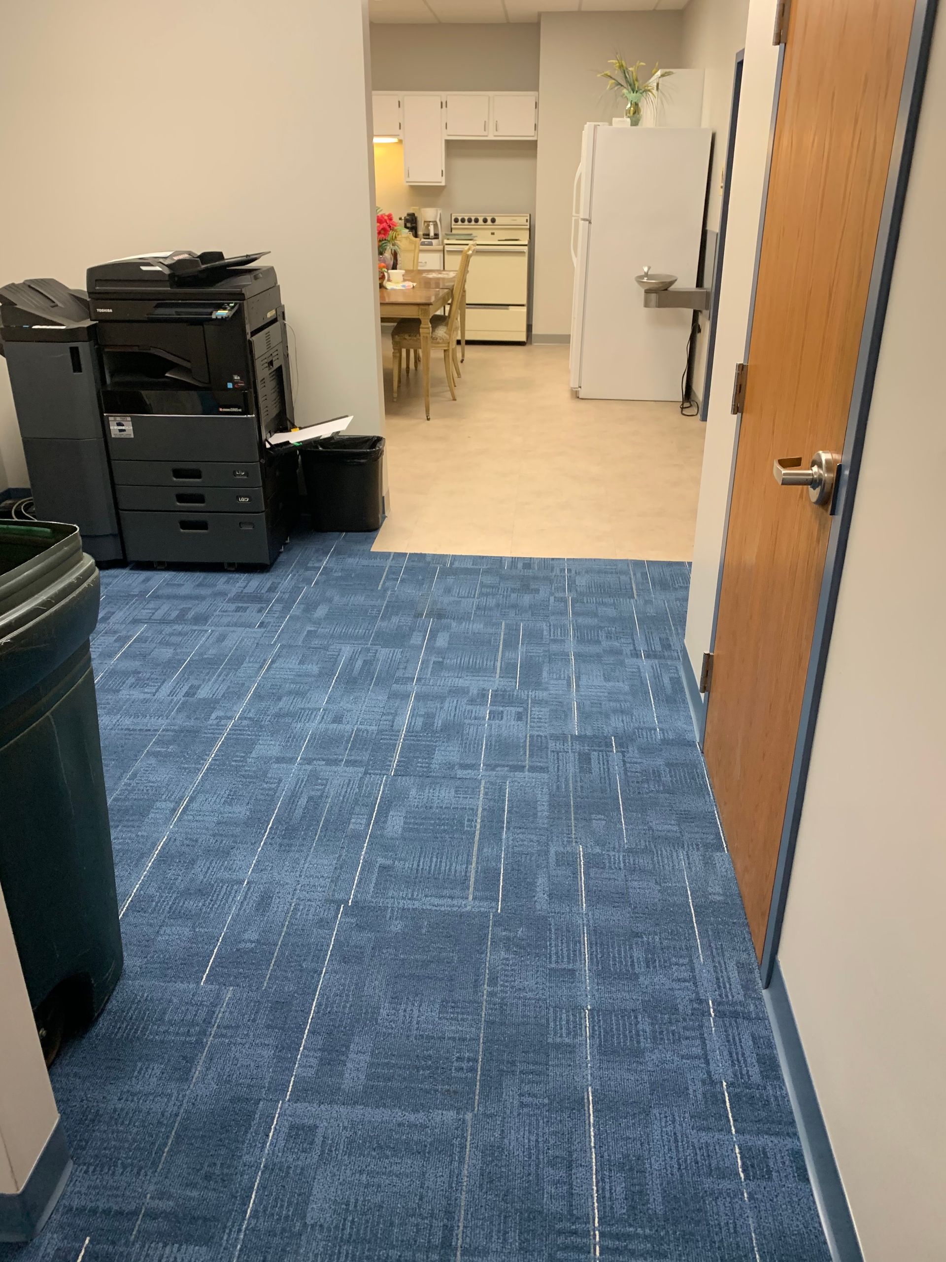 A hallway with a blue carpet and a door leading to a kitchen