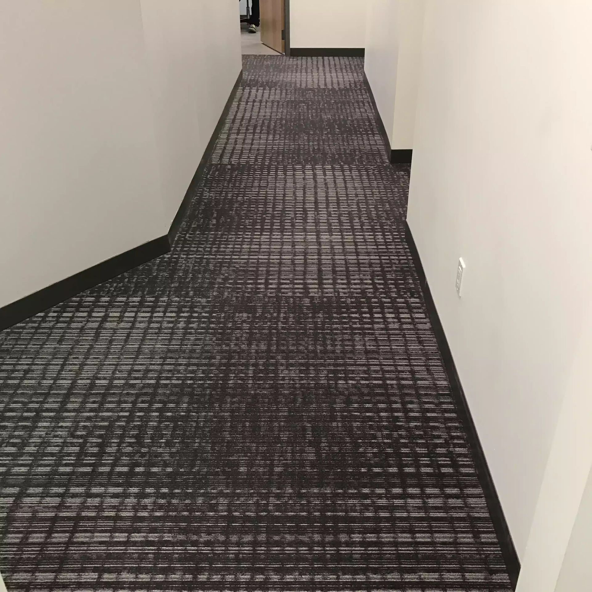 A long hallway with a carpeted floor and a white wall