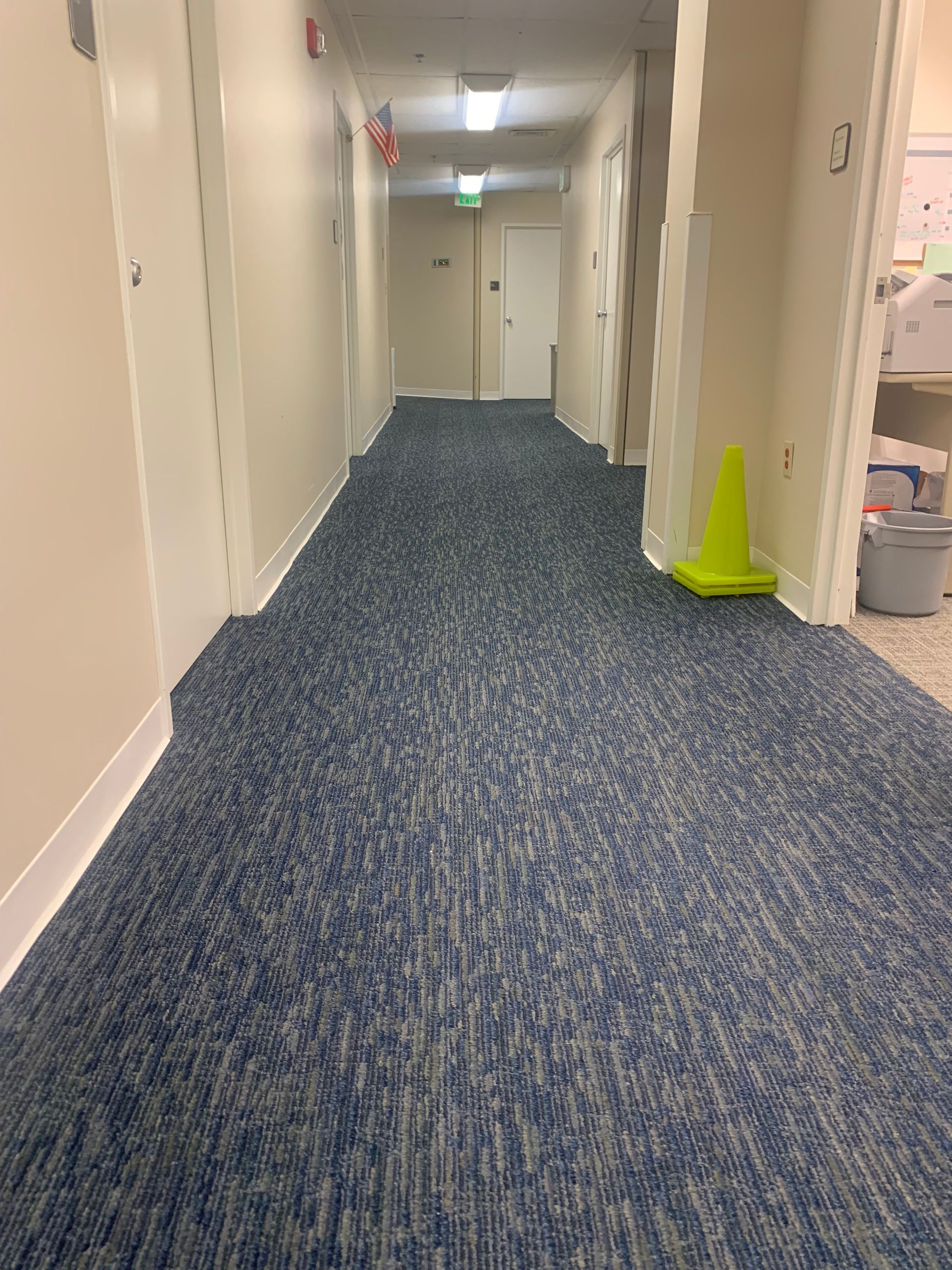 A long hallway with blue carpet and a yellow cone on the floor
