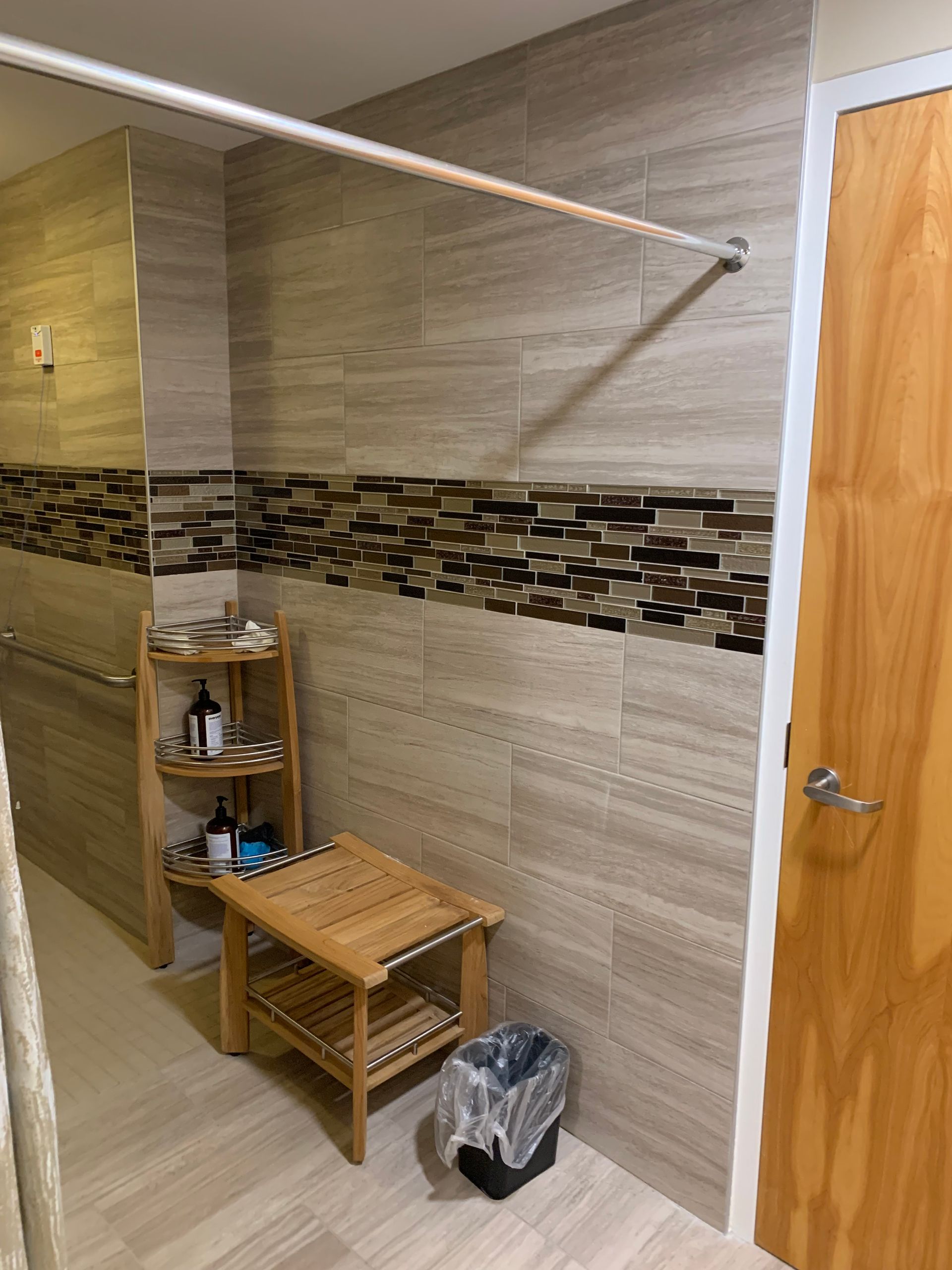 A bathroom with a wooden stool , a shelf, a trash can and a shower curtain