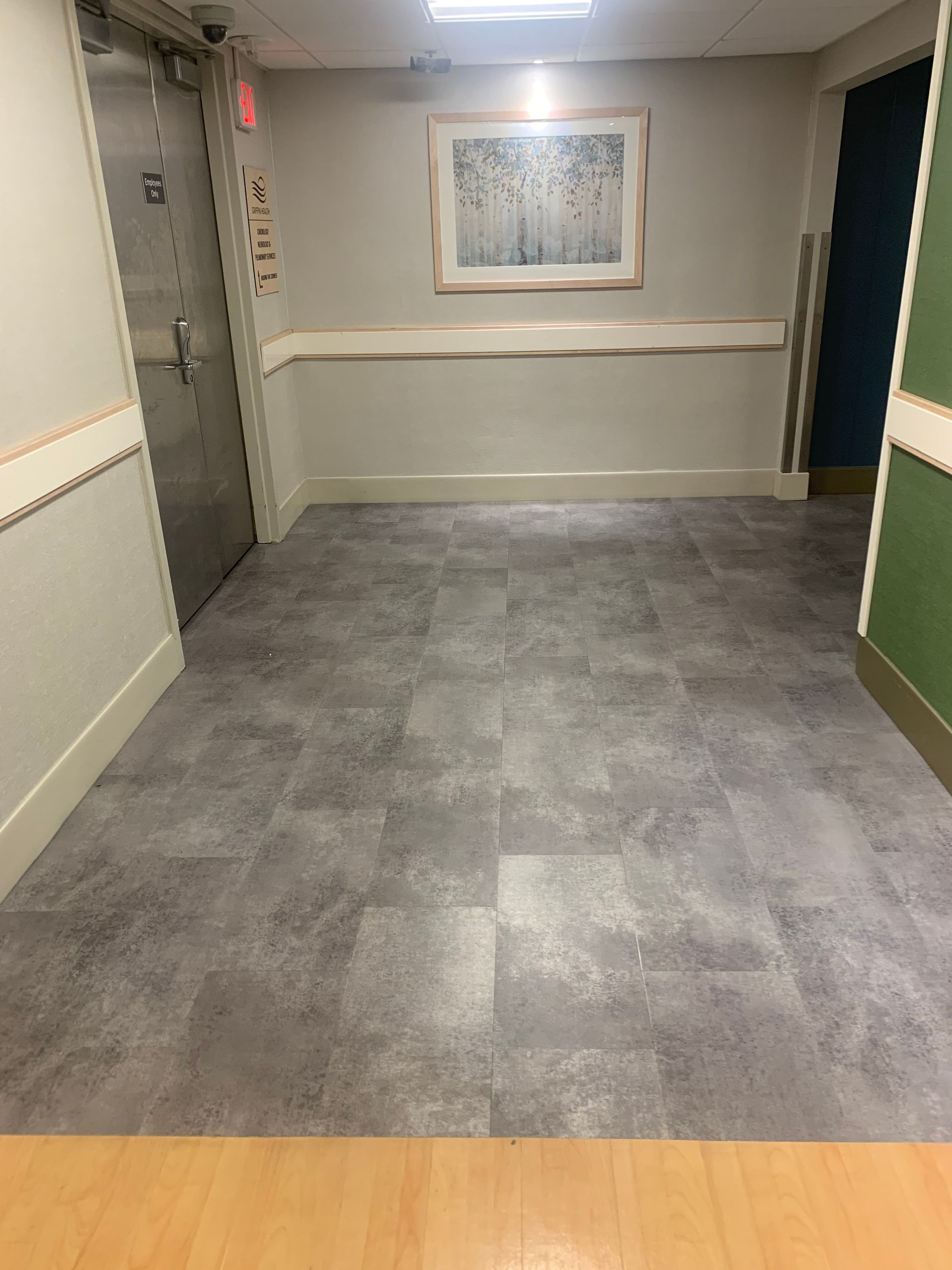 A hallway with a picture on the wall and a gray tile floor.