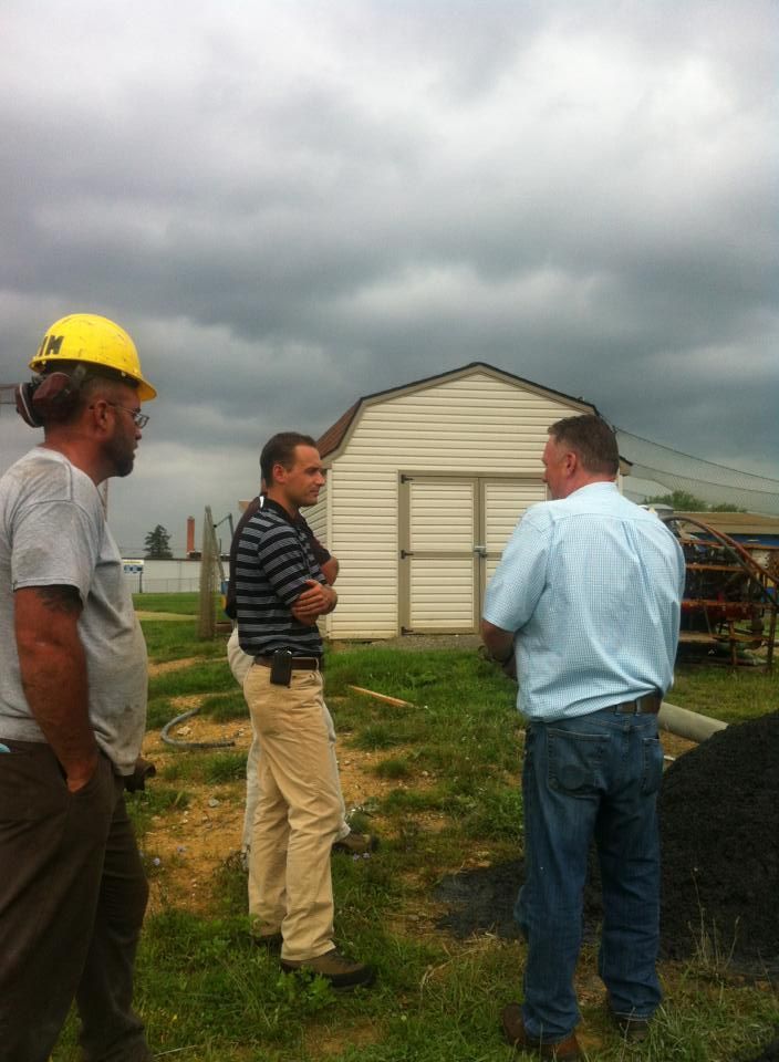 Three men are standing in a field in front of a barn.