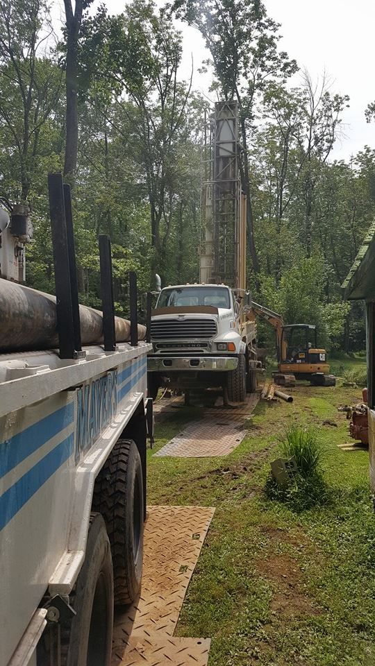 A truck is carrying logs on a trailer in a yard.