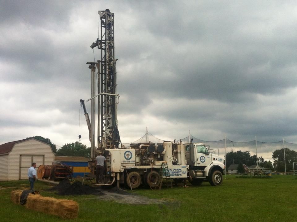 A large white truck with a drilling rig on the back is parked in a grassy field