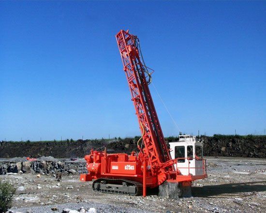 A large red and white machine is sitting on top of a dirt field.