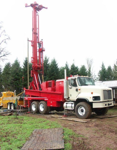 A red and white truck is parked in a field with trees in the background