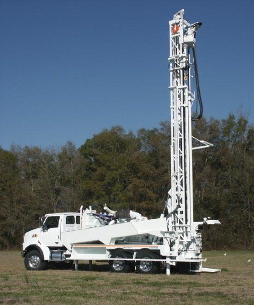 A large white truck is parked in a field with trees in the background