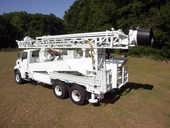 A white truck is parked in a grassy field with trees in the background.