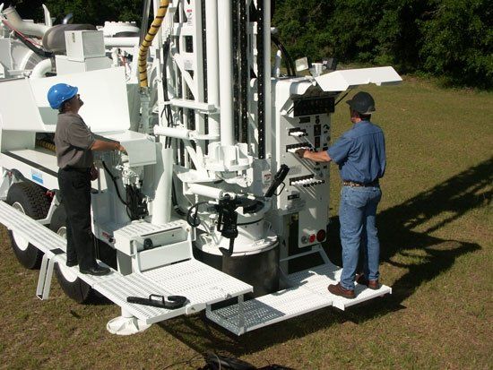 Two men are working on a machine that says ' drill ' on it