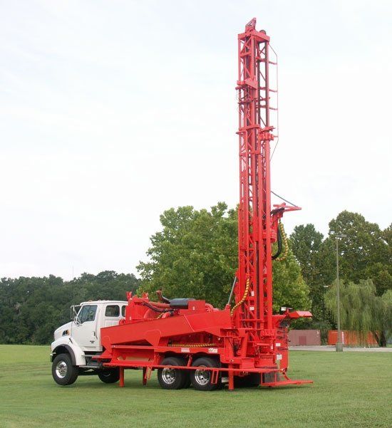 A red truck is parked in a grassy field with trees in the background