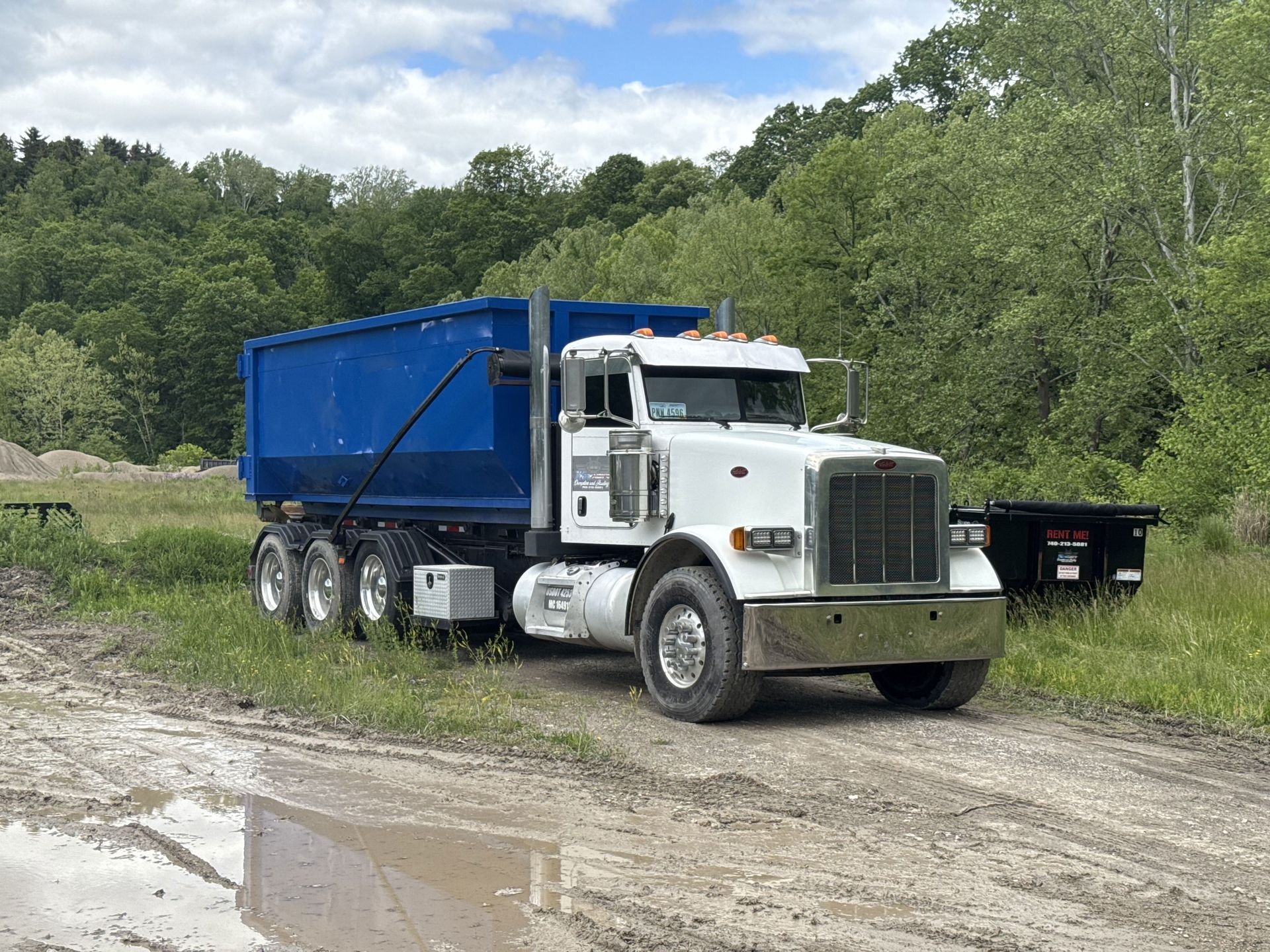 A white dump truck with a blue trailer is parked on a dirt road.