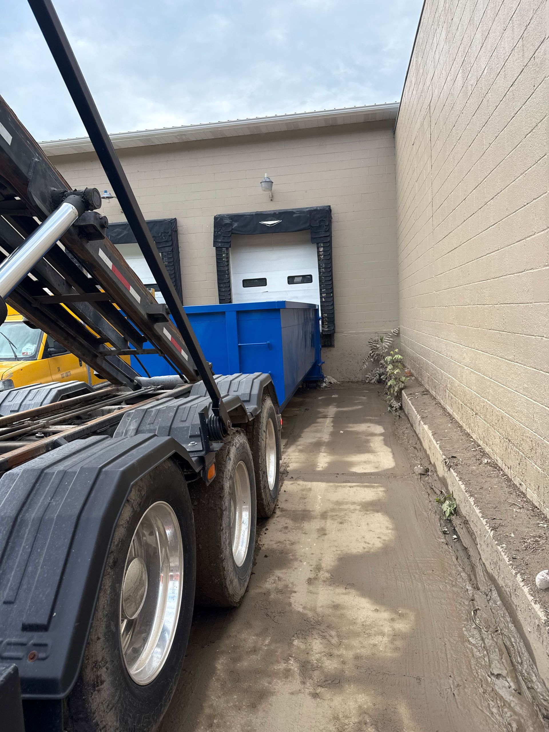 A dump truck is pulling a blue dumpster into a building.