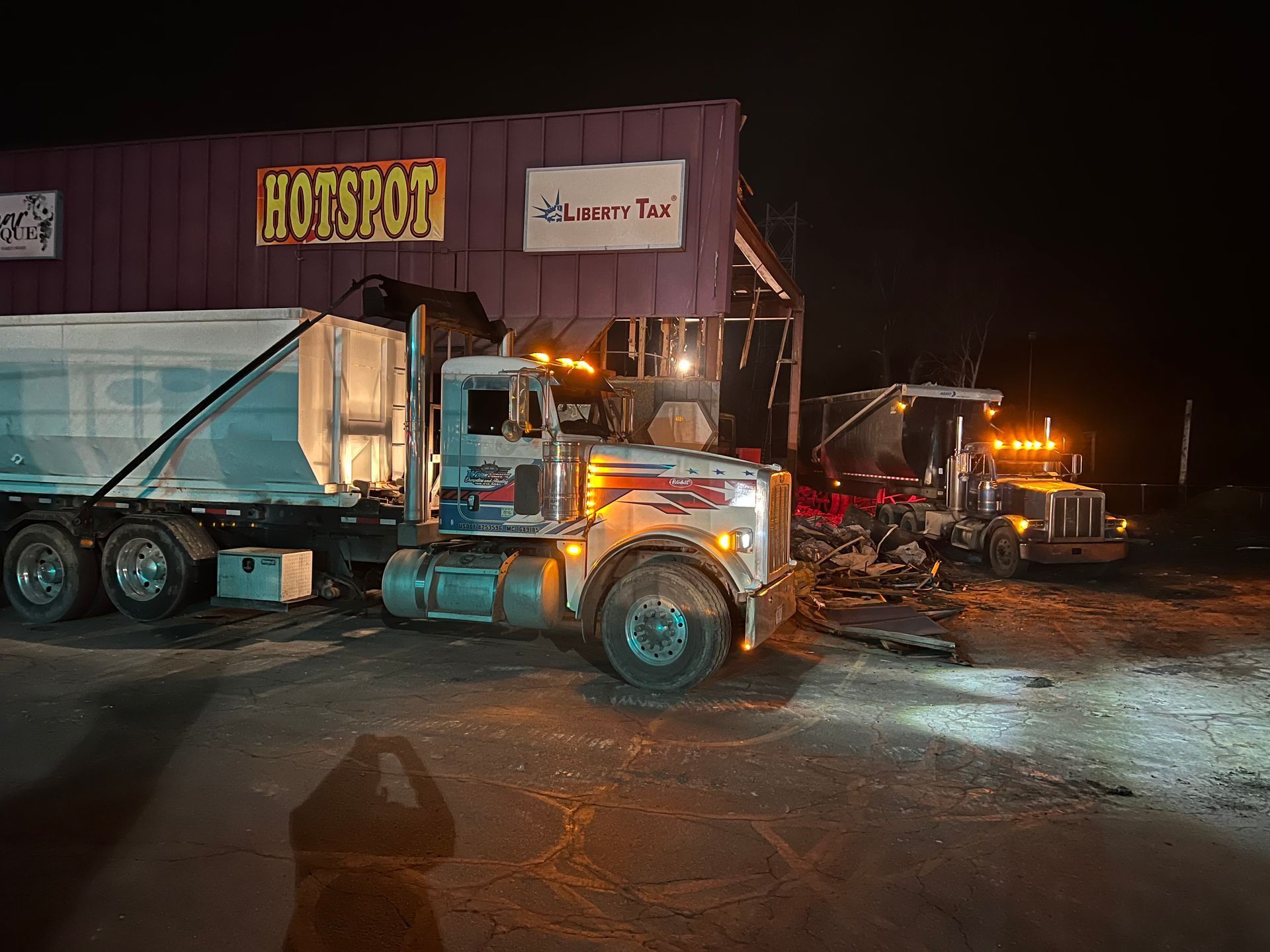 Two semi-trucks parked near a building at night.