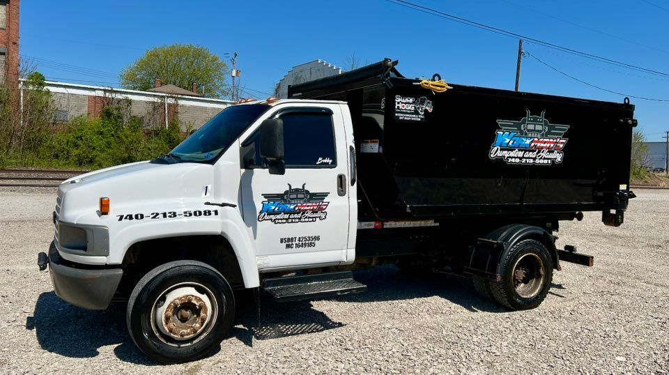 White dump truck with black bed parked on concrete. Company logo and phone number on the side.