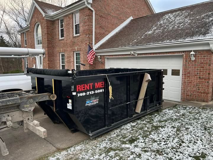 Black dumpster in front of a brick house with an attached garage.