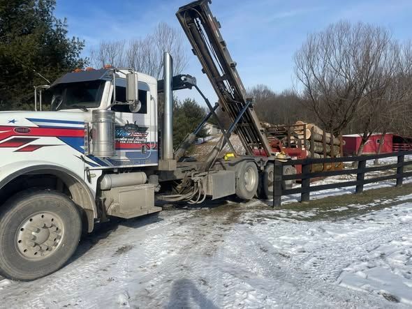 Semi-truck with raised bed by a wooden fence in a snowy area. The truck is white with red and blue accents.